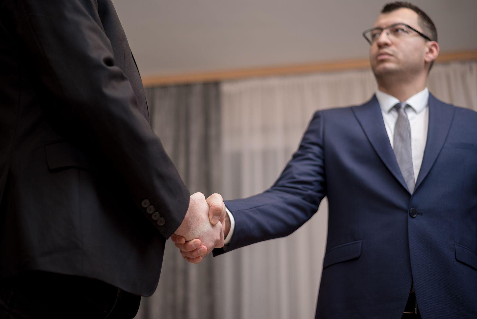 Two businessmen shaking hands across a desk in an office