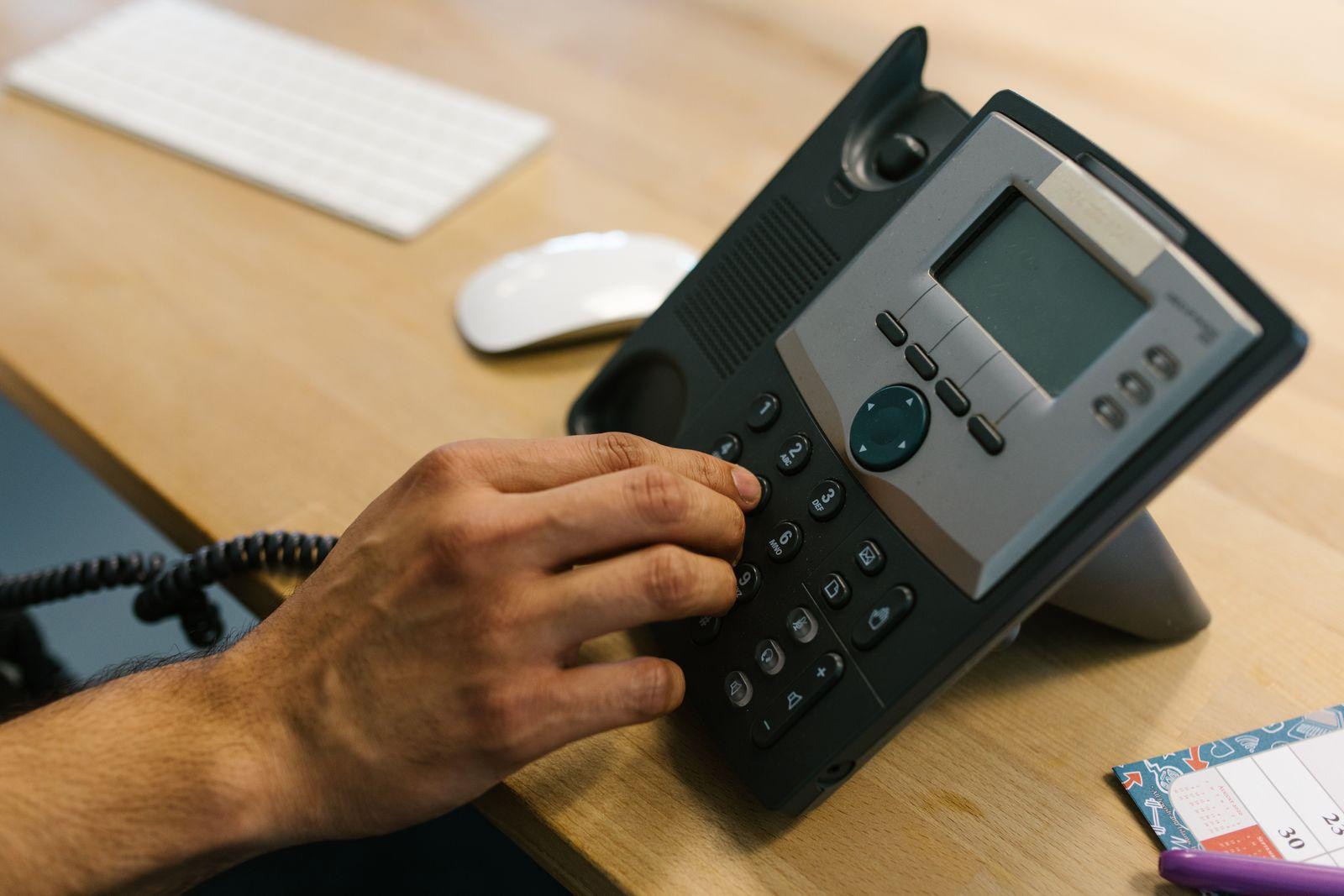 A hand dialing a phone on a wooden office desk